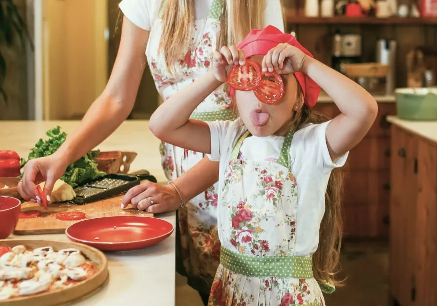 A child holding two tomato slices up to their eyes in a kitchen